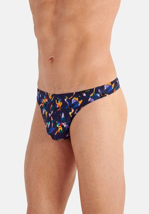 Männlicher Torso mit tief sitzenden Slips mit dunklem Blumenmuster in Blau, Orange, Gelb und Grün auf weißem Hintergrund.