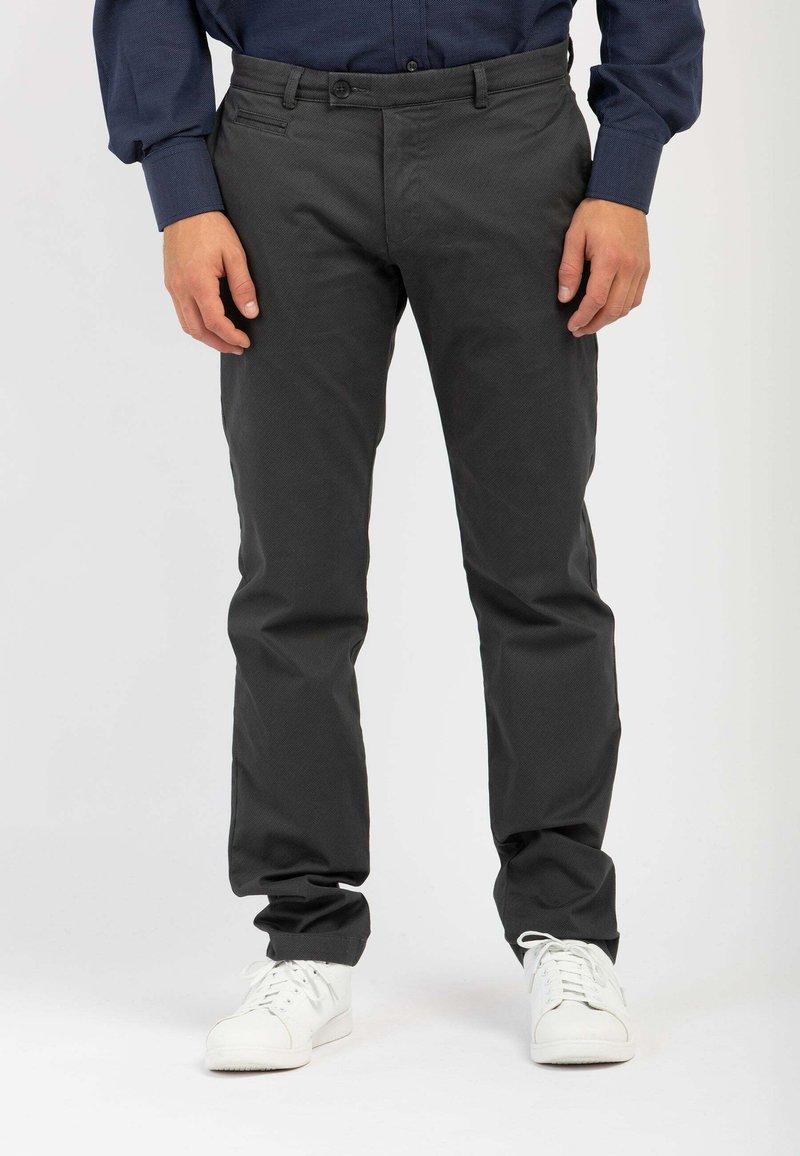 Pantaloni grigi scuri in taglio slim con fascia liscia, due tasche frontali e chiusura con bottone, abbinati a sneakers bianche. Tessuto liscio.