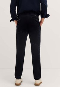 Dark blue corduroy trousers with a straight cut, featuring back pockets and a textured surface. Worn with white sole shoes.