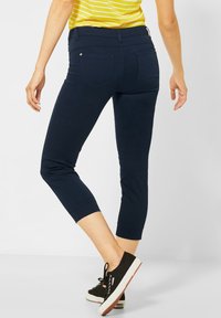 Pantalones cortos azul marino con una textura suave, que presentan dos bolsillos traseros, un diseño ajustado y un dobladillo ajustado. Llevados con zapatillas negras.