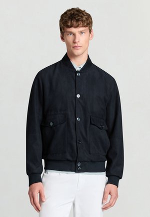 Schwarze Wildlederjacke mit Stehkragen, vorderer Knopfleiste und zwei Brusttaschen. Das Design umfasst gerippte Bündchen und Saum.