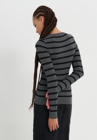 Pull en tricot côtelé gris avec des rayures noires, à manches longues et design ajusté. Il dispose d'un col rond et de poignets de manches allongés.