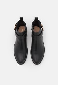 Botas de tobillo de cuero negro con un acabado suave, punta redondeada, tacón bajo y detalle de hebilla lateral. El interior cuenta con una plantilla color marrón.