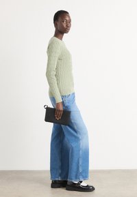 Maglione verde chiaro a maglia, jeans larghi blu, pochette nera e scarpe nere con accenti bianchi. Texture liscia e vestibilità rilassata.