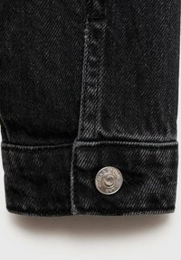Črn denim zapet s srebrno gumbom na pritisk z vgraviranim besedilom, ki prikazuje grobo teksturo in temno tkanino.