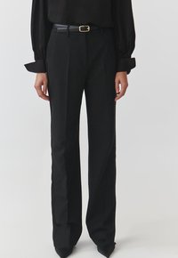 Pantaloni neri sartoriali con vita alta, caratterizzati da pieghe pressate e un design a gamba dritta. Completo con una cintura nera slim e tacchi a punta.