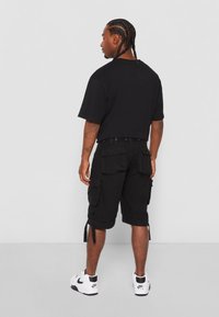 Sort bomulds T-shirt med korte ærmer, parret med sorte cargo shorts med sidelommer og snore, båret med hvide træningssko.