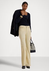 Béžové džíny s širokými nohavicami, prednými vreckami a zlatými kovovými doplnkami, kombinované s priliehavým tmavomodrým tričkom s dlhým rukávom. Drží sa čierna a sivá kabelka.