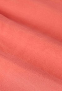 Tissu de couleur corail avec une texture lisse et légèrement brillante, plié pour montrer son drapé fluide et son éclat subtil. Aucun motif ni matériel visible.