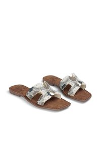 Sandały typu slip-on z teksturowaną białą górą z czarnymi i taupe akcentami, brązowym zamszowym fotelem oraz płaską, elastyczną podeszwą.