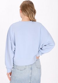 Felpa cropped azzurro chiaro con vestibilità rilassata, polsini a coste e scollatura rotonda. Tessuto testurizzato, abbinata a una gonna di jeans.