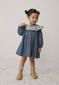 Modré dlouhé šaty s květinovým volánovým límcem, nařaseným pasem a zvonovou sukní. Kombinované s béžovými kotníkovými botami a modrými ponožkami.