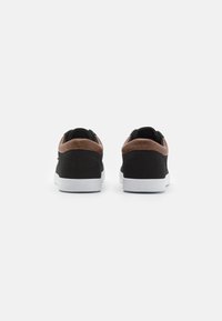 Baskets en toile noires avec des accents en cuir marron, semelles en caoutchouc blanches et un design arrondi. Comprend un contrefort rembourré pour le soutien.