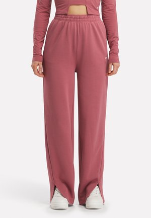 Vrouw draagt hoge taille wijde broek in poederroze met zijinkepingen, gecombineerd met witte sneakers en een bijpassend cropped top met lange mouwen.