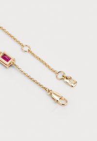 Gouden kettingarmband met een rechthoekige roze edelsteen. Het bevat een kreeftsluiting en een klein label met gegraveerde details.