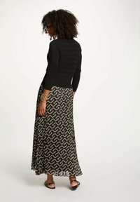 Zwarte, aangesloten trui met geribbeld patroon, gecombineerd met een lange, gestreepte rok in zwart en roomkleur met een golvend ontwerp.