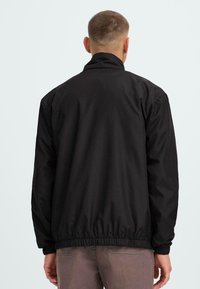 Black, lightweight jacket with a high collar, elastic cuffs, and hem. Smooth texture, minimal design, and no visible hardware or accents.