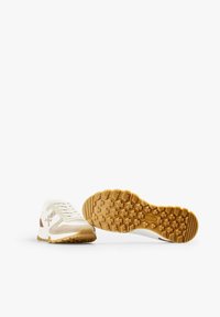 White athletic shoes made of mesh and suede, featuring beige accents, a textured gum rubber sole, and a lace-up design.