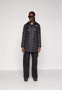 Black puffer coat with zip front and hood, featuring quilted design. Paired with black cargo pants and black shoes.