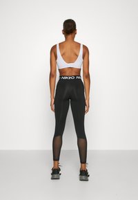 Mustat legginsit, joissa on läpinäkyvät paneelit ja brändätty vyötärö, yhdistettynä vaaleanharmaaseen urheilutoppiin, jossa on matala selkädesign.