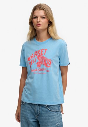 Camiseta de algodón azul claro con estampado gráfico rojo que incluye "MARKET DELI" y diseño de langosta, cuello redondo y mangas cortas.