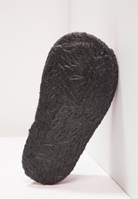 Zwarte rubberen schoenzool met een gestructureerd, gemusterd oppervlak met hoekige ontwerpen. Gebogen vorm, onder een hoek tegen een witte achtergrond.