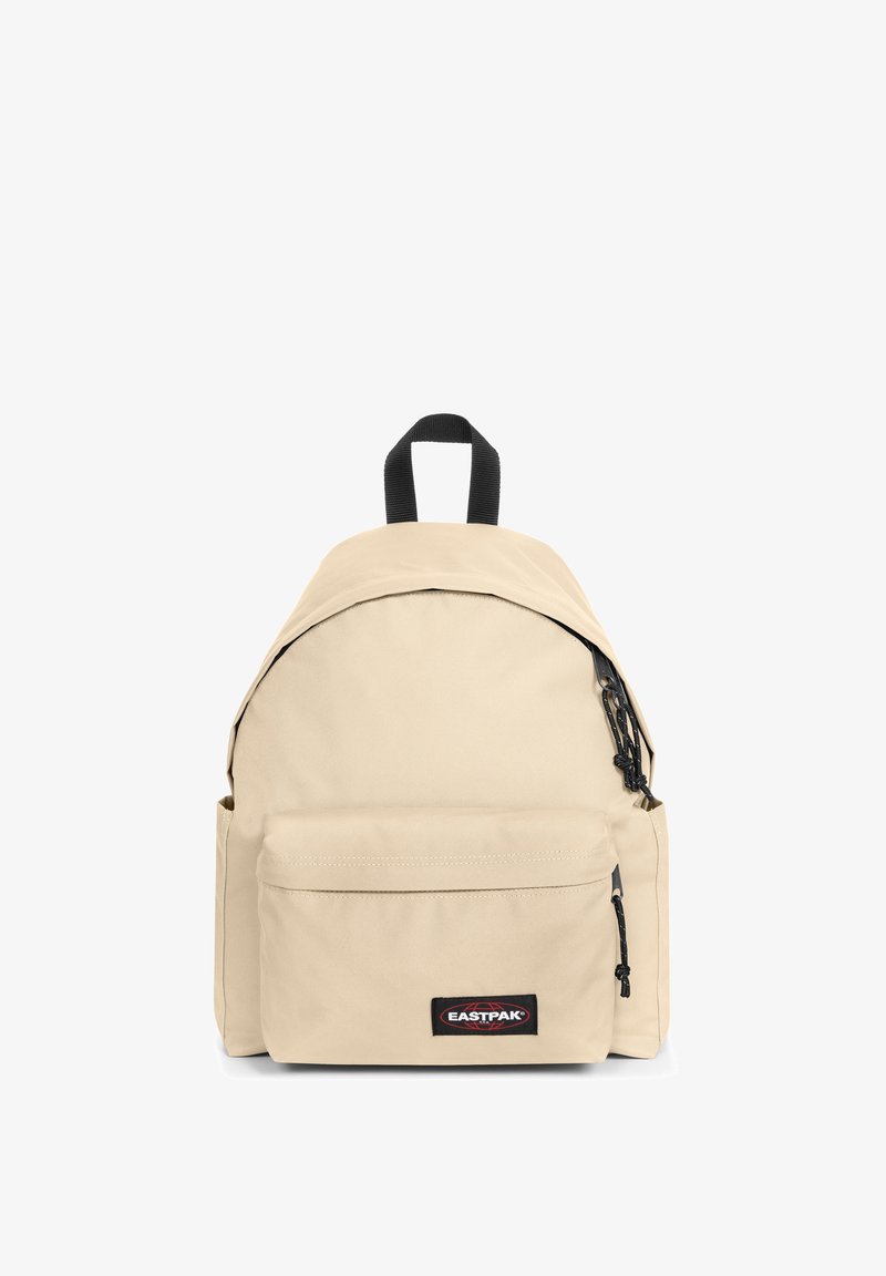 Beige stoffen rugzak met afgeronde vorm, zwarte ritsen, voorvak en een bovenste handvat. Heeft een logopatch aan de voorkant.