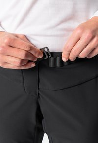 Persoon die een zwarte riem gesp vastmaakt op zwarte broek terwijl hij een witte gemêleerde lange mouw shirt draagt.