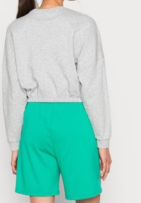 Grå kort sweatshirt med långa ärmar och elastisk nederkant, matchad med turkosa shorts i mjukt material som visar en avslappnad passform.