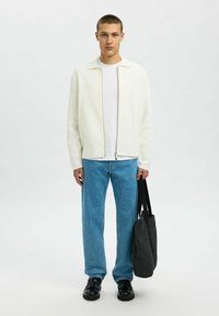 White zip-front jacket, white t-shirt, blue straight-leg jeans, black shoes, and a dark gray tote bag. Minimalist design and clean lines.