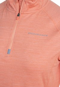 Letvægts quarter-zip pullover i blød, struktureret koralfarvet stof. Features grå logo "ENDURANCE" og kontrastfarvet lynlås for funktionalitet.
