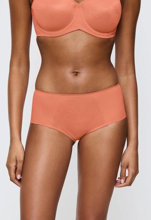 Kobieta ubrana w dopasowany koralowy stanik i figi w stylu hipstera o subtelnym teksturowanym wzorze, pokazana od połowy klatki piersiowej do górnej części ud.