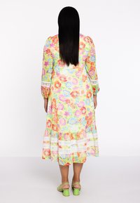 Robe midi florale avec une base jaune ornée de fleurs roses, oranges et bleues, bordure en dentelle blanche à l'ourlet, et manches bouffantes longues.