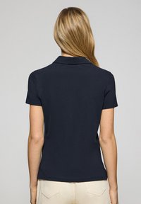Polo shirt bleu marine à manches courtes et col classique, fabriqué en tissu lisse, avec un ourlet droit et des détails minimalistes.