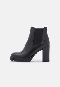 Botte de cheville en cuir noir avec panneaux élastiques sur les côtés, talon épais et semelle crantée. Elle dispose d'une boucle à l'arrière pour un enfilage facile.