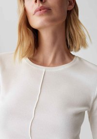 Geripptes, leichtes Langarmoberteil in Off-White. Verfügt über einen Rundhals und ein zentrales Nahtdetail an der Vorderseite für Struktur.