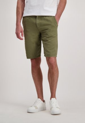 Olijfgroene shorts met een relaxte pasvorm, voorzien van zijzakken en een zachte, gestructureerde stof. Gepaard met witte sneakers.