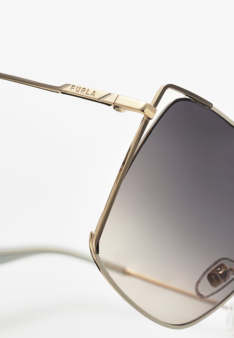 Gafas de sol cuadradas con lentes oscuros degradados y un delgado marco de metal dorado con "FURLA" grabado en la patilla.