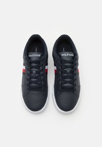 Baskets en cuir bleu marine avec semelles blanches, ornées de rayures rouges et blanches et de lacets noirs. Le logo "HILFIGER" est inscrit sur la languette.