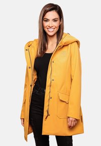 Capa impermeable amarilla con capucha, cierre de cremallera y bolsillos frontales. Presenta una textura suave y detalles de costura en contraste.