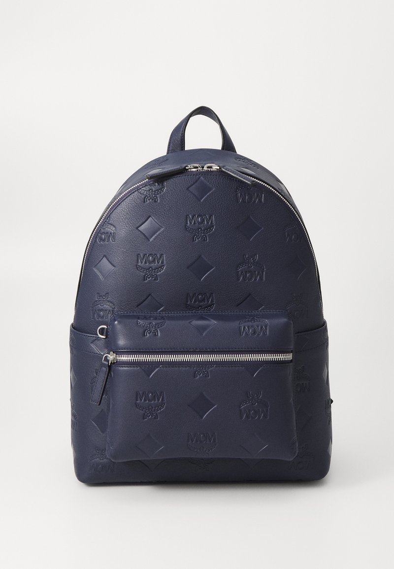 Tengerészkék bőr hátitáska, amely dombornyomott logó mintákkal, kerek formával, felső fogantyúval és elülső cipzáras zsebbel rendelkezik.