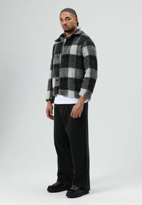 Zwart-grijs geruit faux fur jack met kraag en knoopsluitingen, gedragen over een wit overhemd en gecombineerd met losse zwarte jeans en laarzen.