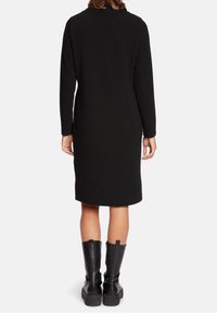 Svart, knälång klänning med långa ärmar och texturerad ribbad tyg; matchad med knähöga boots i svart läder.