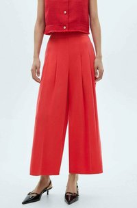 Rode wijde broek met plooien, gecombineerd met een korte rode textuur top. Zwarte puntige hakken met een decoratief accent maken de look compleet.
