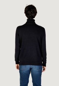 Maglione nero a collo alto realizzato in tessuto morbido, con maniche lunghe e design aderente. Abbinato a jeans blu, visto da dietro.