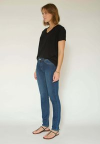 T-shirt noir à col en V, jean skinny bleu et sandales marron à lanières. Le t-shirt est ample et le jean a une ceinture classique.