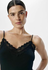 Top nero in satin con pizzo al collo, spalline sottili e texture del tessuto liscia. Primo piano che si concentra sulla parte superiore dell'indumento e sul pizzo dettagliato.