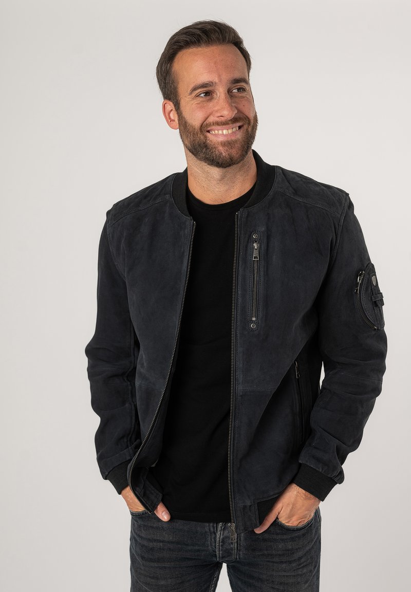 Donkerblauwe suède herenjack met ribgebreide mouwen en kraag; voorzien van meerdere ritszakken en een gestructureerd oppervlak.