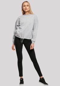 Grijze sweatshirt met lange mouwen, een trekkoord aan de onderkant en een relaxte pasvorm, gecombineerd met zwarte skinny jeans en zwarte high-top sneakers.