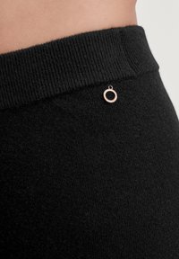 Zwarte gebreide leggings met een gestructureerde tailleband en een kleine metalen accessoire in de vorm van een cirkel aan de zijkant.